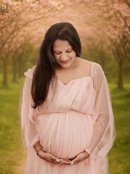 A close-up portrait of a mom-to-be looking down at her bump, wearing a delicate pink gown with sheer sleeves.