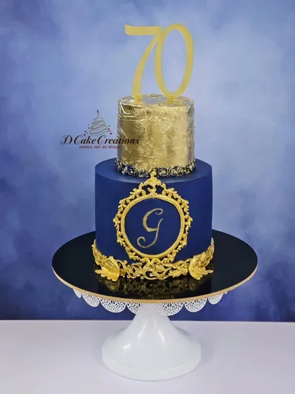 A regal 70th birthday cake in royal blue and gold. This two-tier cake features a gold leaf top tier and an ornate monogram, perfect for a grand milestone.