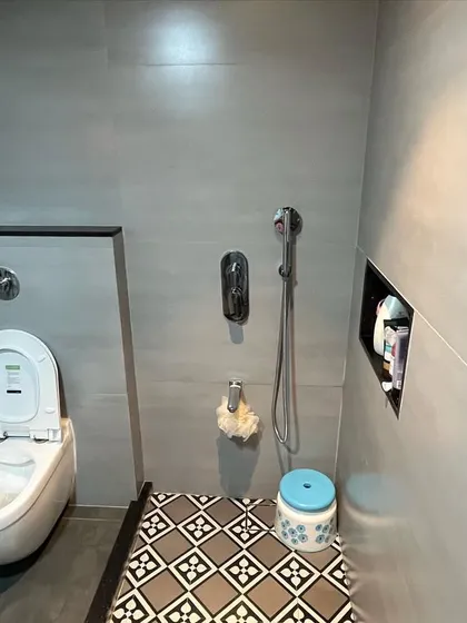 A minimalist bathroom design featuring grey wall tiles and patterned floor tiles in the shower area. The wall-mounted toilet and concealed cistern create a clean, uncluttered look.