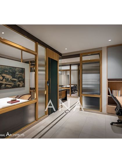 The general workstation area in the Jain Cosphere Office. The design features simple floating wooden tops, beige overhead cabinets, and solid dark green doors with brass details to match the overall theme.