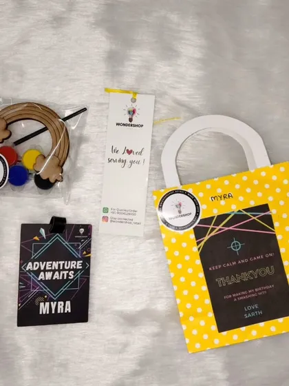 A complete return gift set for a laser tag party. It includes a personalized "Adventure Awaits" tag and a rainbow craft kit, all packed in a cheerful bag with a custom thank you note.