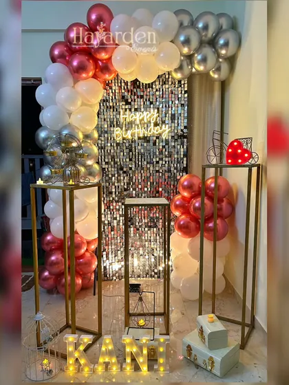 An elegant home party setup with a silver sequin backdrop and a balloon arch in metallic red and silver. The tall pedestals and marquee letters add a touch of class.