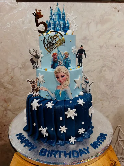 A grand three-tier Frozen cake for a 5th birthday. This impressive cake features Elsa, Anna, Olaf, and Sven, with a beautiful ice castle and edible snowflakes creating a winter wonderland.