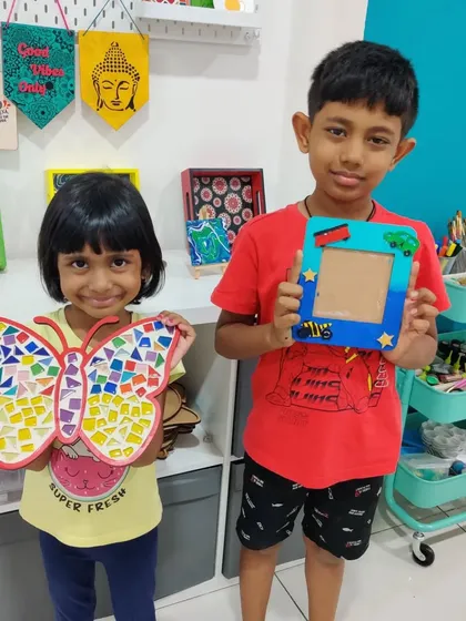 Siblings proudly showing off the mosaic butterfly and photo frame they made as a birthday gift for their dad.