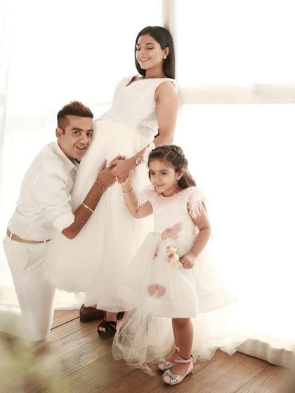 A lovely family portrait celebrating the anticipation of a new arrival. The natural light from the window creates a soft, dreamy effect, perfect for capturing these special family moments.