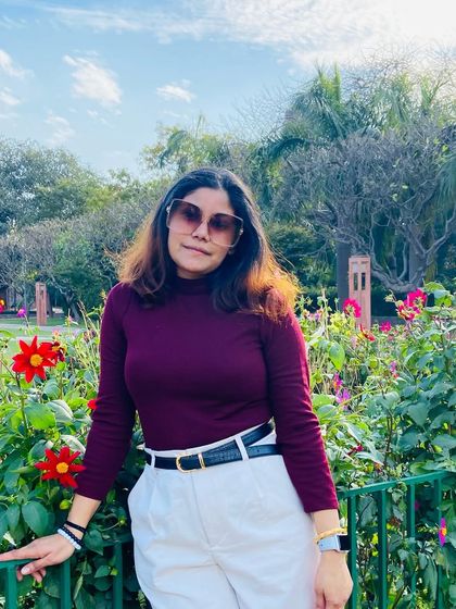Posing amongst the flowers at Sunder Nursery. The deep burgundy of my top contrasts beautifully with the vibrant red flowers and my crisp white pants, creating a stylish and seasonal look.