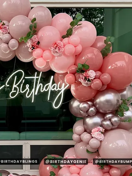 A close-up of the dusty rose balloon arch, showing the delicate floral accents and the glowing neon sign.
