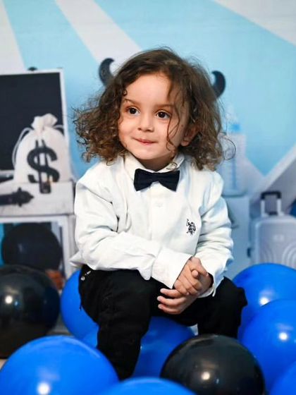 Posed among blue and black balloons, this little boy looks confident in his Boss Baby setup, complete with a prop briefcase full of money in the background.