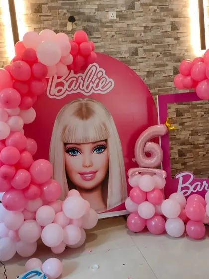 A Barbie theme with a large-scale character backdrop and a pink balloon arch. This setup also includes a Barbie photo booth frame.