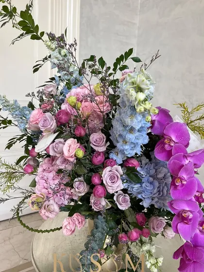Inspired by vintage romantic novels, this arrangement transports you to a sweet daydream. It combines Kenyan Delphiniums, Dutch Phalaenopsis orchids, and sky-blue hydrangeas with berry and lilac roses for a truly fairytale feel.
