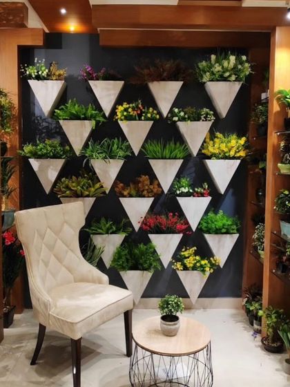 A feature wall with a grid of modern, triangular wall-mounted planters. Each planter is filled with a different type of small artificial plant for a varied and artistic display.