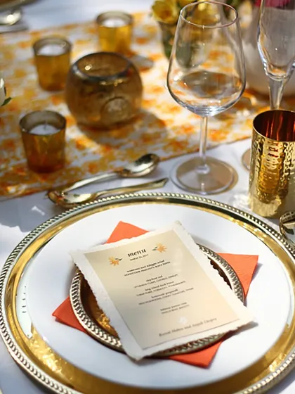 A close-up of a place setting with a custom menu card on a gold-rimmed charger plate. We personalize every aspect of the dining experience to make your intimate sit-down dinners truly special.