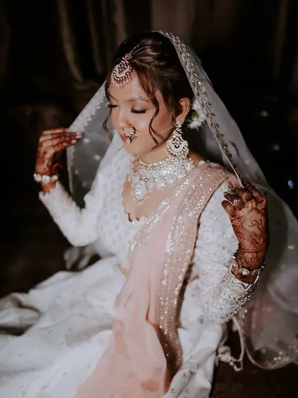 This bride looks serene and beautiful in her white and peach lehenga. The makeup is soft and romantic, with a focus on glowing skin and gently defined eyes, perfect for her elegant attire.