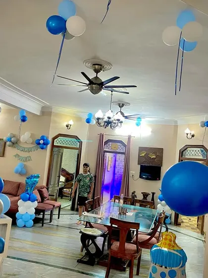 A full room view of a welcome home party for a baby boy. The decorations include a central balloon ring, pillars, and balloons on the ceiling, all in a coordinated blue and white theme.