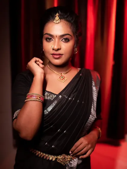 A model posing in a black saree, with a confident and bold expression.