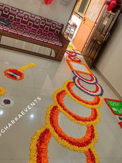 A traditional and colorful welcome home decoration for a baby. The floor is decorated with intricate flower rangoli patterns, creating a vibrant and auspicious pathway.
