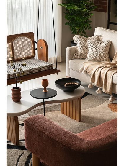 A close-up of the living area, showing the custom reversible cane swing and organic-shaped coffee table. The combination of textures, from the woven pillows to the fluted table base, creates a cozy and inviting setting.