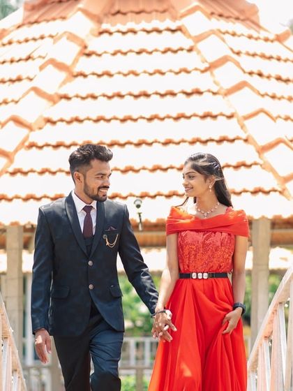A classic pre-wedding photo of a couple walking on a bridge. The red lace-bodice gown is a timeless and romantic choice.