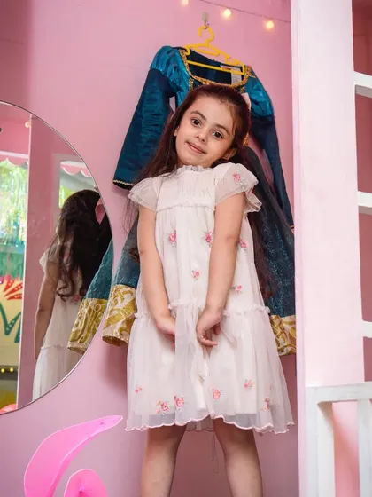A sweet girl posing in our pink playhouse, with a princess dress hanging in the background, ready for the next costume change.