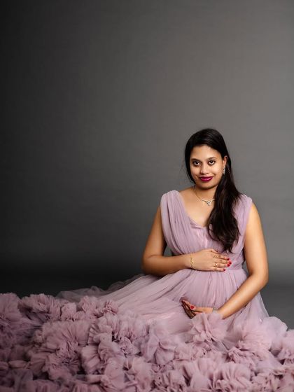 A lovely seated portrait of a mother-to-be in a flowing lavender gown. Her gentle smile and the soft texture of the dress create a serene and dreamy atmosphere.