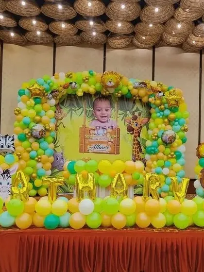 A jungle-themed birthday stage with a photo backdrop and the name 'ATHARV' in foil balloons.