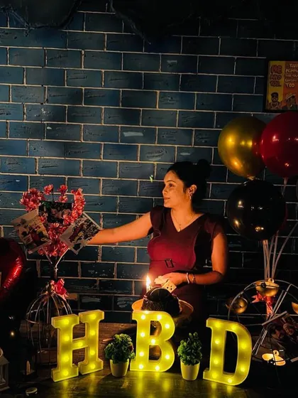 A candid shot of the birthday girl with her cake and custom table decor against a cool blue brick wall, lit by a single candle and the glow of the marquee letters.