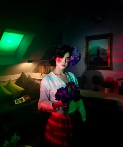 A moody, atmospheric portrait using colored lighting. The makeup is subtle but designed to react to the red and green lights, creating a painterly and cinematic feel.