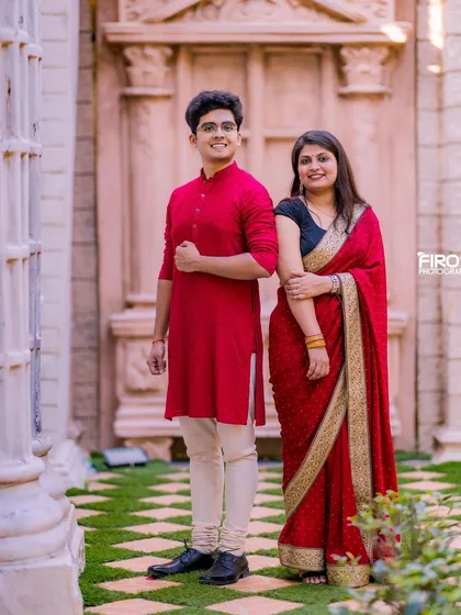 A stylish portrait of a couple in traditional red outfits against a grand stone doorway.
