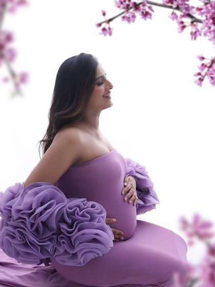 A close-up filled with joy. The soft smile and gentle hold on her belly, framed by delicate blossoms, make this a truly heartwarming and beautiful portrait.