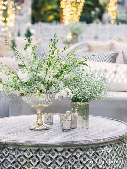 A table centerpiece featuring baby's breath and white gladioli in a silver pedestal vase. The decor is kept elegant and understated to complement the grandeur of the surroundings.