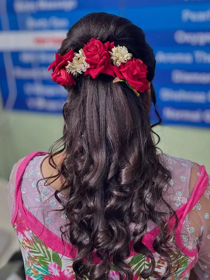 A romantic hairstyle featuring soft curls and a beautiful arrangement of red roses. This half-updo is perfect for a reception or engagement party, adding a touch of classic elegance.
