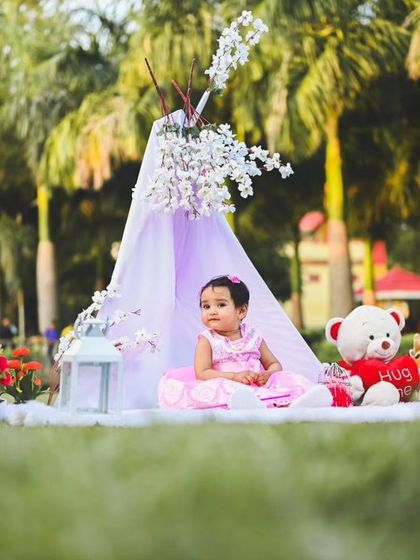 A full view of the whimsical outdoor setup, complete with a teepee, 'ONE' sign, balloons, and lanterns, creating a perfect backdrop for a first birthday portrait.