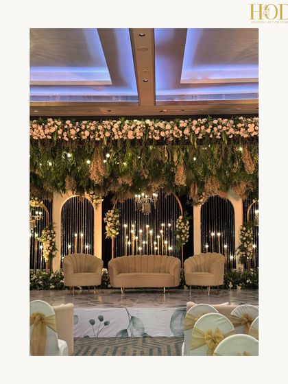 A beautiful stage setup with a lush canopy of hanging greenery and flowers, with a backdrop of modern arches and candle-like lights.