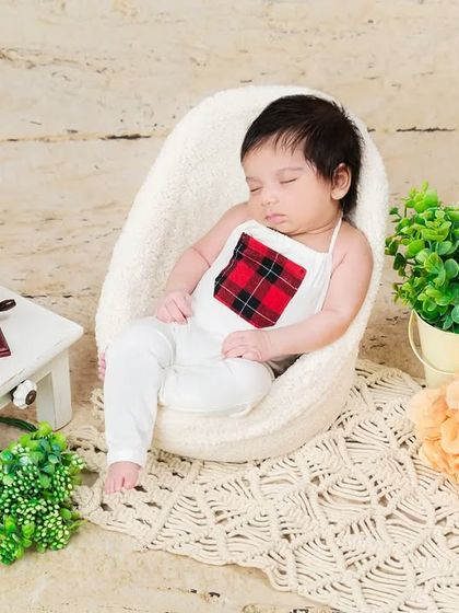 A newborn sleeps peacefully in a miniature armchair next to a vintage-style gramophone prop. A unique and charming setup for a timeless photo.