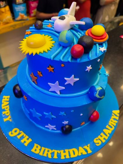 A two-tier space theme cake for a 9th birthday. This cake takes you on a journey through the solar system with fondant planets, stars, and a spaceship, creating an out-of-this-world celebration.