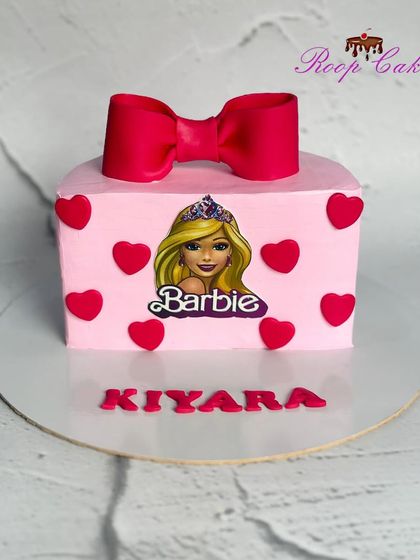 A sweet half-birthday cake with a Barbie theme. This pink square cake is decorated with red hearts, a big red bow, and a Barbie topper for little Kiyara.