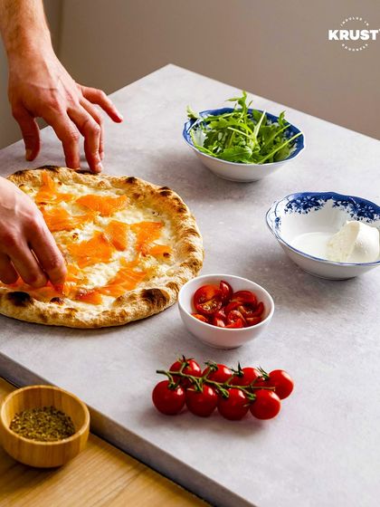 Your pizza, your rules. This shot shows a participant adding salmon and other gourmet toppings to their pizza, showcasing the creative freedom you get in our workshops.
