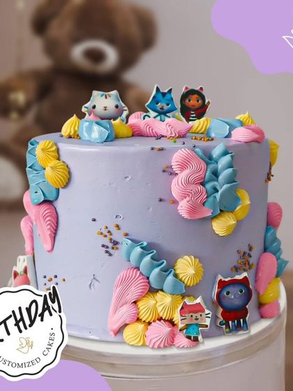 A colorful and cute cake featuring characters from Gabby's Dollhouse. The pastel purple frosting and playful details make this a perfect treat for a fan.