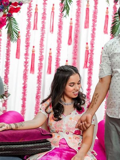 A father holds his daughter's hand during her mehendi ceremony, his own hand bearing a tattoo of her wedding date. A truly special bond.