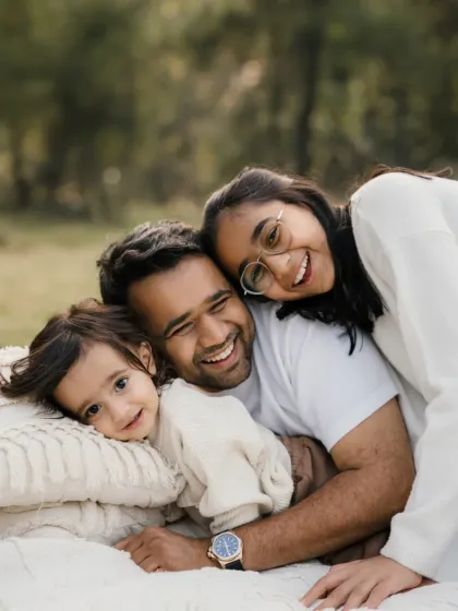A family of four cuddles together on a blanket outdoors. This photo is full of warmth and shows the close bond between parents and their two children.