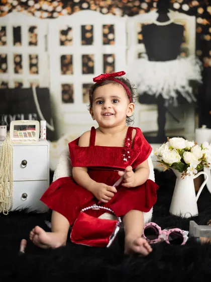 Dressed in red velvet, this little girl is a true fashion queen, surrounded by makeup and accessories.