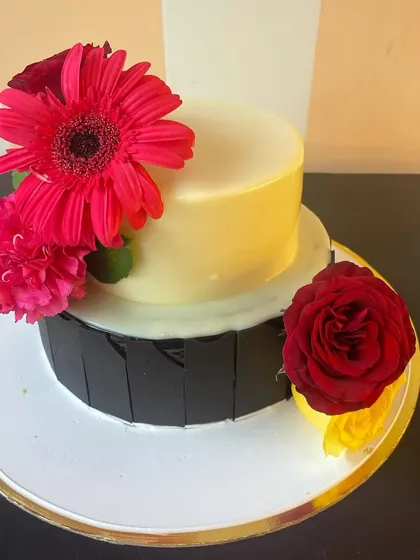 A unique two-tier cake featuring a dark chocolate bottom tier and a white chocolate top tier. The design is elevated with fresh, vibrant flowers, creating a beautiful contrast of color and texture.