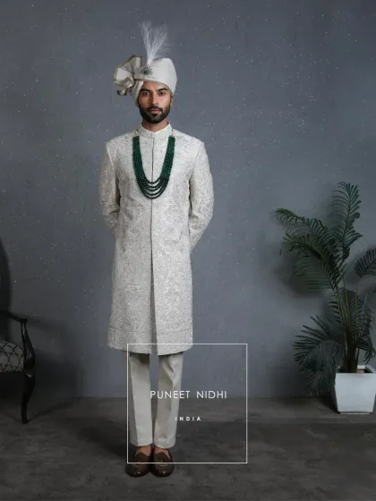More than fabric, it is devotion. An ivory paneled sherwani where resham and zari aariwork bloom into timeless floral vines, accented with an emerald mala for a touch of royal color.
