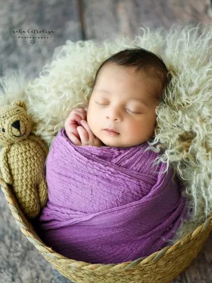 A close-up of the baby in the purple wrap, showing their tiny fingers resting on their cheek.