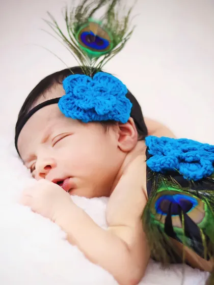 A close-up portrait of the newborn in the peacock theme, focusing on the delicate facial features and the colorful props.