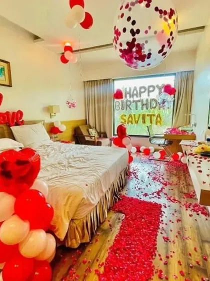 A birthday surprise in a hotel room with 'LOVE' and 'HAPPY BIRTHDAY' foil balloons, and a path of rose petals.