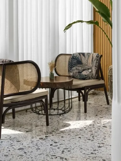 This quiet seating nook features dark wood rattan chairs against a backdrop of sheer white curtains, creating a soft, diffused light. It’s an intimate corner perfect for conversation, combining classic materials with modern comfort.