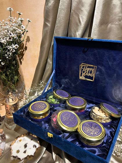 A royal blue velvet box for Diwali, holding several jars of dry fruits. The gold "Happy Diwali" cutout adds a touch of luxury.