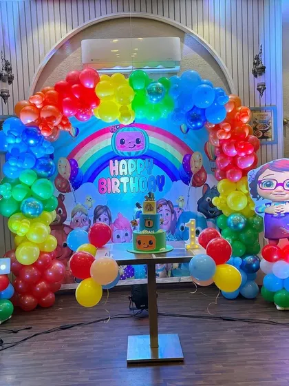 The complete Cocomelon party setup, including a themed cake table, character cutouts, and a large light-up number '1'.