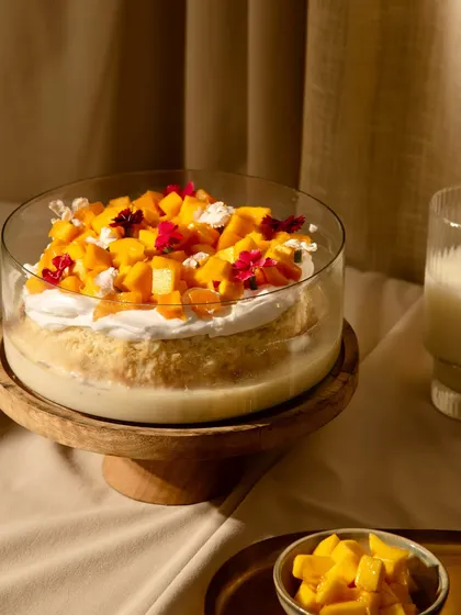 A beautifully shot Mango Tres Leches, served on a wooden stand. This seasonal special is a light and refreshing dessert perfect for warm days.